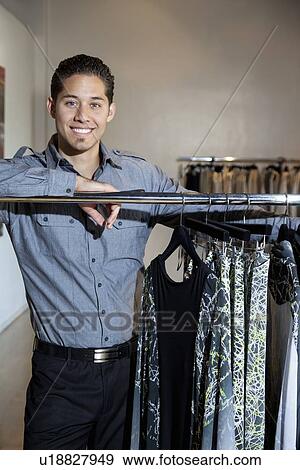 Portrait of a happy young man standing by clothes rack in fashion boutique View Large Photo Image Stock Photo - Portrait of a happy young man standing by clothes rack in fashion boutique. Fotosearch