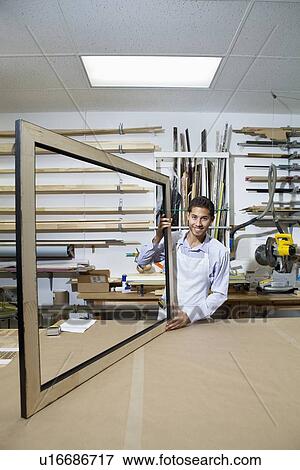 Stock Photo - Portrait of a happy young man working on big picture frame in workshop. Fotosearch