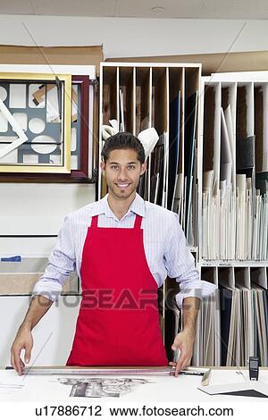Stock Image - Portrait of a happy young skilled worker standing with meter stick in workshop. Fotosearch