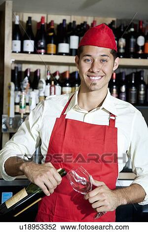 Stock Image - Portrait of a happy young waiter with bottle and glass. Fotosearch