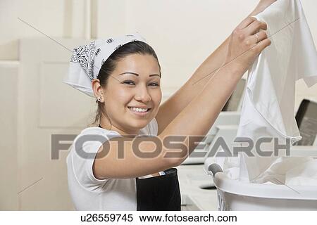 Stock Photography - Portrait of a happy young woman holding cloth in Laundromat. Fotosearch