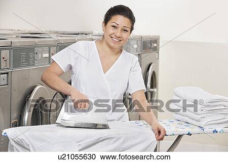 Stock Image - Portrait of a happy young woman ironing clothes in Laundromat. Fotosearch