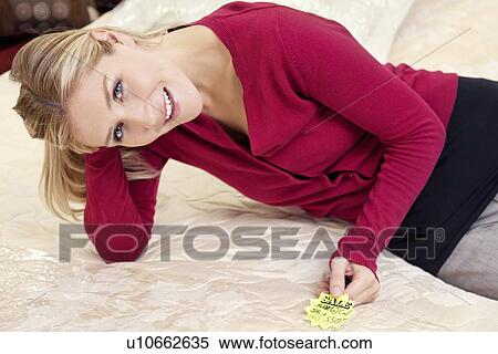 Stock Photography - Portrait of a happy young woman reclining on mattress with price tag. Fotosearch