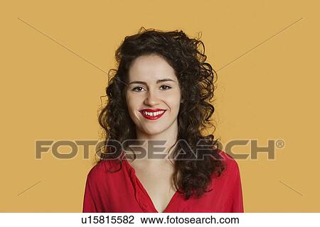 Stock Image - Portrait of a happy young woman with curly hair over colored background. Fotosearch