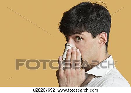 Stock Image - Portrait of a man blowing his nose over colored background. Fotosearch