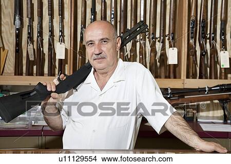 Picture - Portrait of a mature man with rifle on shoulder in gun store. Fotosearch