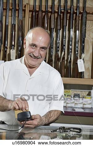 Portrait of a mature merchant with credit card reader in gun shop View Large Photo Image Picture - Portrait of a mature merchant with credit card reader in gun shop. Fotosearch