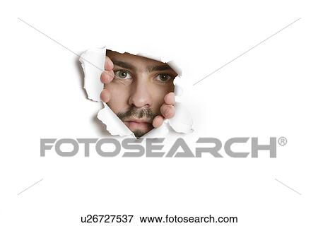 Stock Photo - Portrait of a mid adult Caucasian man peeking from ripped paper hole. Fotosearch