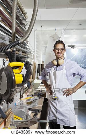 Stock Photo - Portrait of a skilled worker standing with hands on hips in workshop. Fotosearch