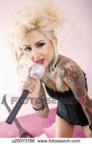 Stock Photograph - Portrait of a tattooed blond woman singing with microphone. Fotosearch
