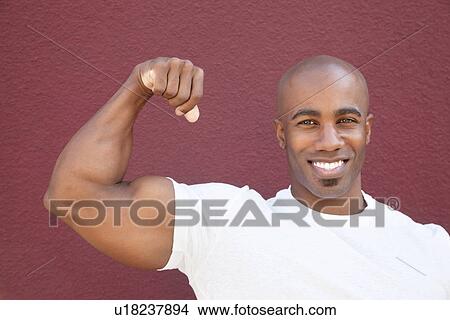 Picture - Portrait of a young African American man flexing muscles over colored background. Fotosearch