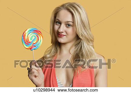 Portrait of a young blond woman holding lollipop over colored background View Large Photo Image Picture - Portrait of a young blond woman holding lollipop over colored background. Fotosearch