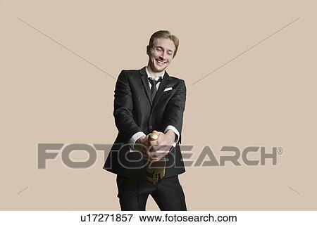 Portrait of a young businessman uncorking champagne over colored background View Large Photo Image Stock Photo - Portrait of a young businessman uncorking champagne over colored background. Fotosearch