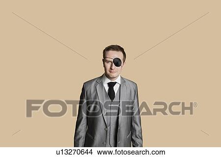 Picture - Portrait of a young businessman with eye patch over colored background. Fotosearch