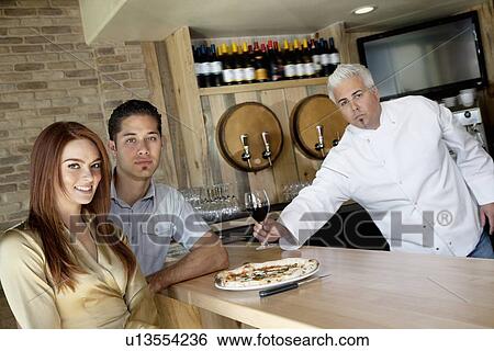 Portrait of a young couple with chef holding wine glass View Large Photo Image Stock Photograph - Portrait of a young couple with chef holding wine glass. Fotosearch