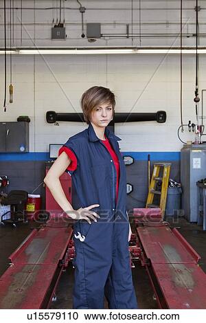 Stock Image - Portrait of a young female mechanic standing with hand on hip in car workshop. Fotosearch