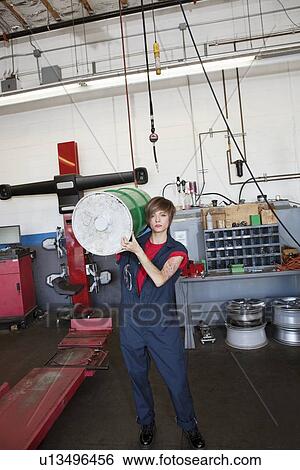 Stock Photograph - Portrait of a young female mechanic carrying oil drum on shoulder in auto repair garage. Fotosearch