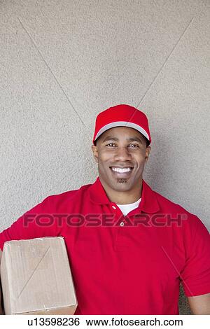 Portrait of a young man holding delivery box against wall View Large Photo Image Stock Photograph - Portrait of a young man holding delivery box against wall. Fotosearch