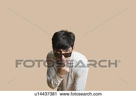 Stock Image - Portrait of a young man wearing sunglasses with hand on chin over colored background. Fotosearch
