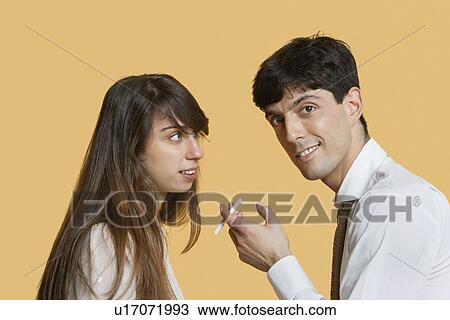 Stock Image - Portrait of a young man with cigarette while woman looking at him over colored background. Fotosearch