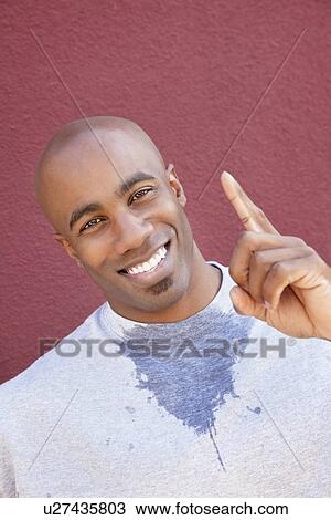 Stock Image - Portrait of a young man with finger pointing upwards over colored background. Fotosearch