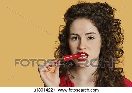 Portrait of a young woman biting red chili pepper over colored background View Large Photo Image Stock Photo - Portrait of a young woman biting red chili pepper over colored background. Fotosearch