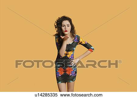 Stock Photography - Portrait of a young woman blowing kisses over colored background. Fotosearch