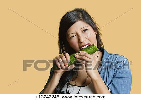 Portrait of a young woman eating cucumber over colored background View Large Photo Image Stock Photograph - Portrait of a young woman eating cucumber over colored background. Fotosearch