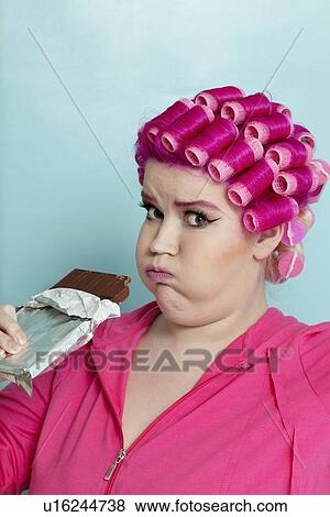 Portrait of a young woman making faces while holding chocolate bar over colored background View Large Photo Image Stock Photo - Portrait of a young woman making faces while holding chocolate bar over colored background. Fotosearch