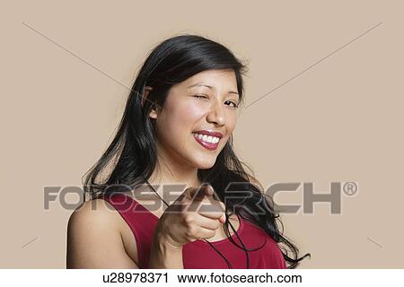 Portrait of a young woman pointing while winking over colored background View Large Photo Image Stock Image - Portrait of a young woman pointing while winking over colored background. Fotosearch
