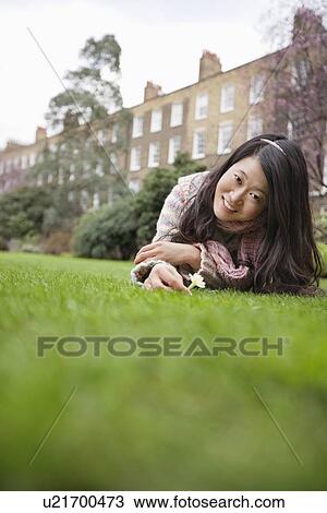 Stock Image - Portrait of a young woman with flower lying lawn in front of building. Fotosearch