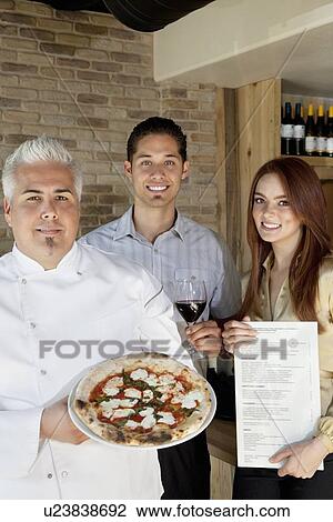 Portrait of happy chef holding pizza with young couple View Large Photo Image Stock Image - Portrait of happy chef holding pizza with young couple. Fotosearch