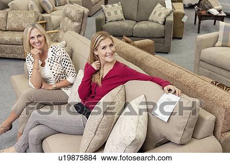 Portrait of happy mother and daughter sitting on sofa in furniture store View Large Photo Image Picture - Portrait of happy mother and daughter sitting on sofa in furniture store. Fotosearch