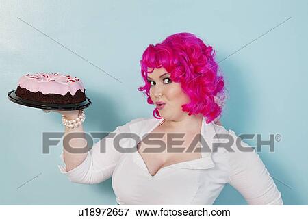 Stock Photo - Portrait of happy woman showing cake over colored background. Fotosearch