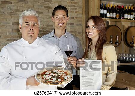 Stock Photo - Portrait of happy young couple with chef holding pizza. Fotosearch