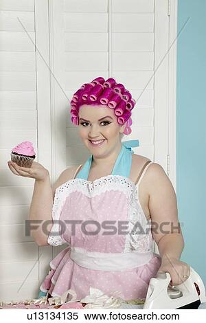 Portrait of happy young woman holding cupcake while ironing View Large Photo Image Stock Photography - Portrait of happy young woman holding cupcake while ironing. Fotosearch