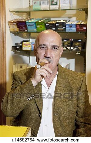Picture - Portrait of mature tobacco store owner smoking cigar. Fotosearch