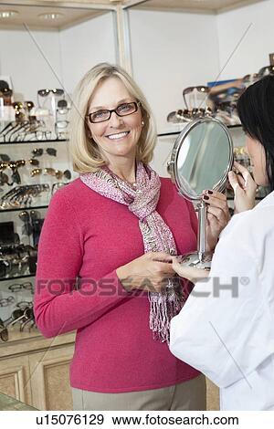 Portrait of senior woman wearing glasses while optician holding mirror View Large Photo Image Stock Photo - Portrait of senior woman wearing glasses while optician holding mirror. Fotosearch