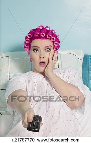 Portrait of shocked woman holding remote with hair curlers sitting on bed View Large Photo Image Stock Image - Portrait of shocked woman holding remote with hair curlers sitting on bed. Fotosearch
