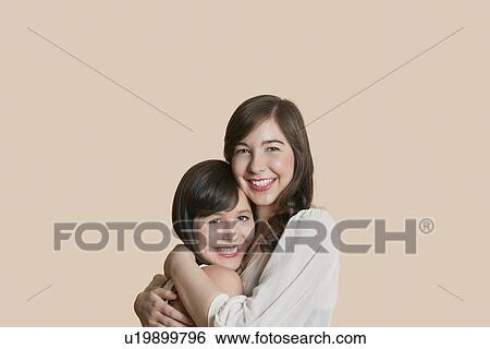 Stock Photograph - Portrait of young female friends hugging over colored background. Fotosearch