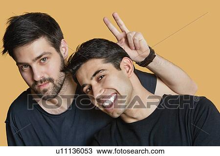 Portrait of young male friends with peace sign over colored background View Large Photo Image Stock Image - Portrait of young male friends with peace sign over colored background. Fotosearch