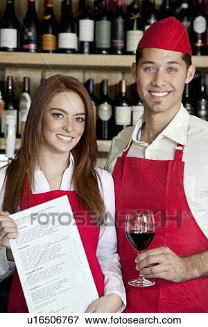 Stock Photo - Portrait of young wait staff with wine glass and menu card in bar. Fotosearch