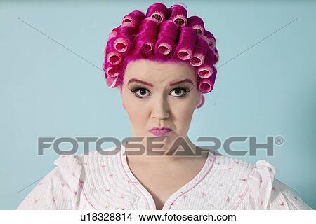 Portrait of young woman grimacing with hair curlers over colored background View Large Photo Image Picture - Portrait of young woman grimacing with hair curlers over colored background. Fotosearch