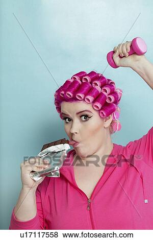 Portrait of young woman licking chocolate bar while light dumbbell over colored background View Large Photo Image Stock Photo - Portrait of young woman licking chocolate bar while light dumbbell over colored background. Fotosearch