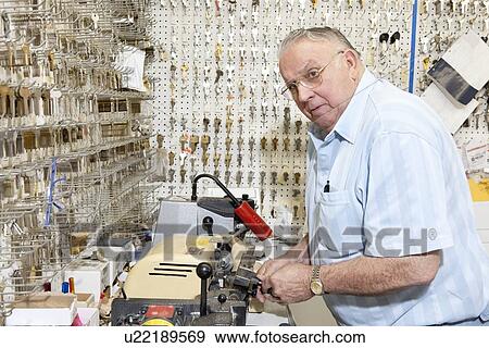 Stock Photo - Senior locksmith looking away while making key in store. Fotosearch