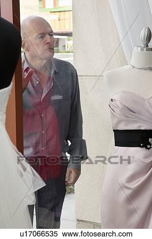 Stock Photography - Senior man looking at wedding dress displayed on window in bridal store. Fotosearch
