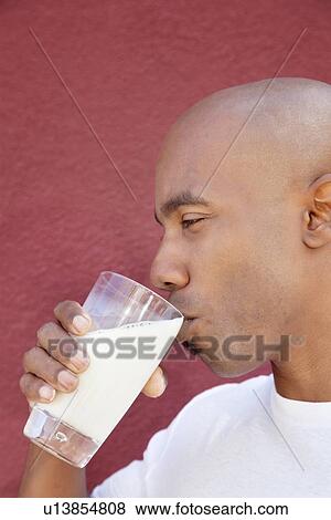 Stock Photo - Side view of an African American man drinking milk over colored background. Fotosearch