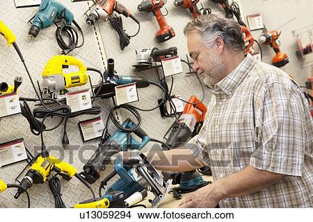 Side view of mature salesperson looking at electric saw View Large Photo Image Picture - Side view of mature salesperson looking at electric saw. Fotosearch