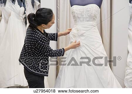Stock Photo - Side view of mature woman adjusting bridal dress in boutique. Fotosearch
