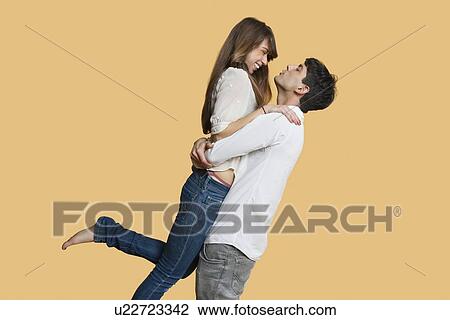 Side view of young couple looking at each other while man carrying girlfriend over colored background View Large Photo Image Stock Image - Side view of young couple looking at each other while man carrying girlfriend over colored background. Fotosearch